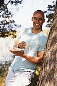 Young man standing by tree with crostini and glass of water