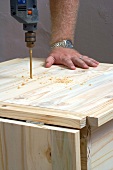 Man drilling a hole in a piece of wooden furniture