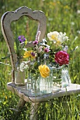Verschiedene Blumen in Gläsern und Flaschen auf Holzstuhl