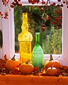 Pumpkins, coloured bottles & rose hip branches at window