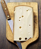 A piece of Appenzeller cheese with knife on chopping board