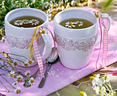 Tee aus Kamillenblüten in zwei Bechern mit Bändern
