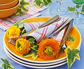 Yellow ranunculus in napkins with cutlery on pile of plates