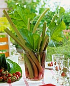 Bunch of rhubarb in glass vase, strawberries and glasses