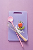 Chopping board, kitchen spoon, whisk, salt, rocket and tomato