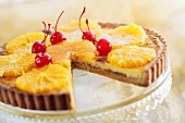 Orange tart with cocktail cherries, a piece removed