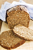 Wholemeal rye bread, partly sliced, on chopping board with tea towel
