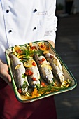 Chef holding baked fish with lemon, vegetables and dill