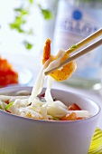 Chopsticks taking prawn and rice noodle out of soup