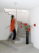 Woman walking up a modern, purist staircase and decorative poppies in black vase