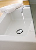 Water running into designer washbasin from wall-mounted tap