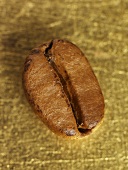 Eine Kaffeebohne auf goldenem Untergrund (Nahaufnahme)