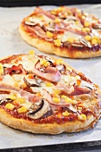 Pizzas topped with ham, sweetcorn and button mushrooms on baking tray