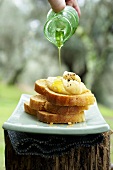 Crostini with creamed beans being drizzled with oil