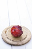 A red plum on a round wooden board