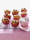 Lots of apple and cranberry muffins on a wire rack with icing sugar