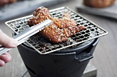 Turning sesame chicken wing on table grill with barbecue tongs