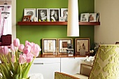 Modern cabinet with matching wooden shelf holding family photos against green-painted wall