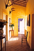 Kräftig gelb getönter Hausflur im mediterranen Stil mit zierlichen Stilmöbeln auf dem Ziegelboden und Geweihen unter der Holzdecke