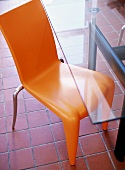 Orange plastic chair and modern glass table on terracotta tiles