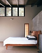 Purist bedroom with double bed and standard lamp against half-height exposed concrete wall