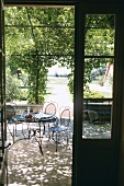 Blick auf eine Gartenterrasse, mit schattenspendender Pergola und filigranen Metallmöbeln, Weinkaraffe und Weingläser