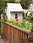 Dekoriertes Gartenhäuschen mit bunten Wimpeln hinter Gartenblumen und Holzbrücke