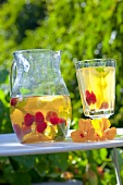 Iced tea with raspberries in a jug and a glass on a garden table