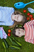 Zwei Mädchen liegen auf der Wiese umgeben von Gemüse