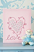 Handmade picture with heart & embroidery behind teddy bear dressed as ballerina