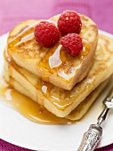 Heart-shaped pancakes with maple syrup and raspberries