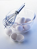 White eggs in a glass bowl, whisk on bowl