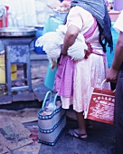 Frau hält einen lebenden Hahn unter dem Arm auf einem Markt