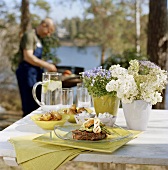 Barbecued dishes on garden table, man barbecuing behind