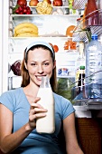 Young woman with milk bottle in front of open fridge