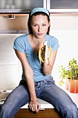 Young woman eating a banana in the kitchen