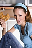 Young woman sitting in kitchen holding a croissant