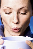 Young woman blowing on hot drink in cup