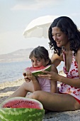 Mother and daughter eating watermelon on beach