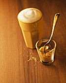 Milky coffee in light brown beaker and glass of sugar