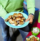 Man holding plate of grilled chicken legs