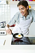 Young man frying an egg on hob