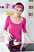 Woman at cooker holding frying pan with fried egg