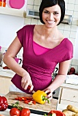 Smiling young woman in kitchen slicing vegetables
