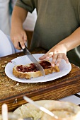 Child's hands cutting a slice of bread & jam with a knife
