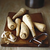 Parsnips with vegetable peeler on wooden board