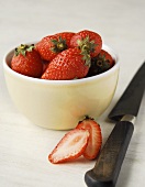 Strawberries in a bowl with halved strawberry and knife
