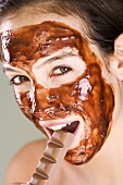 Woman with chocolate face mask eating a bar of chocolate