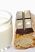A piece of chocolate, baguette and a glass of milk