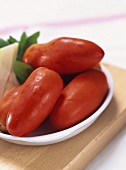 Plum tomatoes in white dish on wooden board